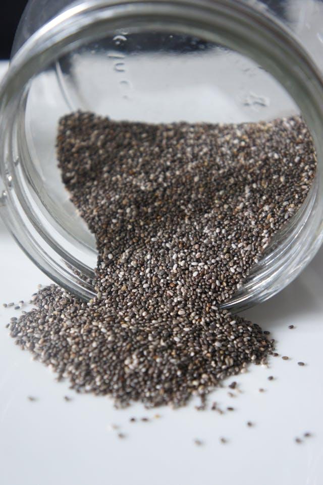 Graines de chia sortant d'un bocal transparent couché
