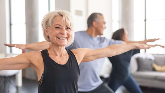 Femme senior avec débardeur noir et bras étendus qui fait du sport et sourit avec un homme et une femme dans la même position en arrière-plan