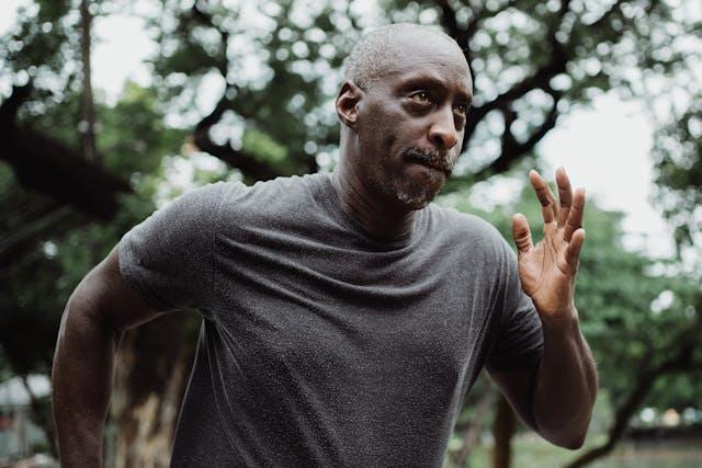 Homme senior noir avec tee-shirt gris foncé qui court avec des arbres en arrière-plan