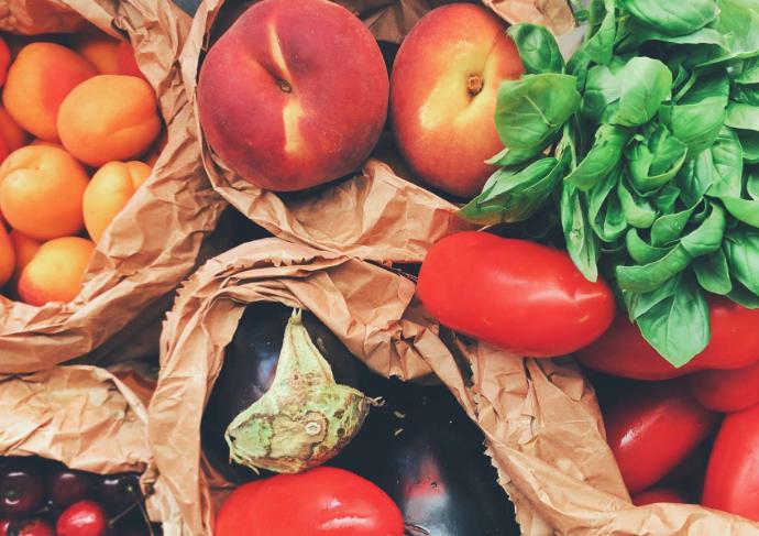 Abricots, cerises, pêches, aubergines, tomates et basilic vus de haut dans des sacs en papier beige