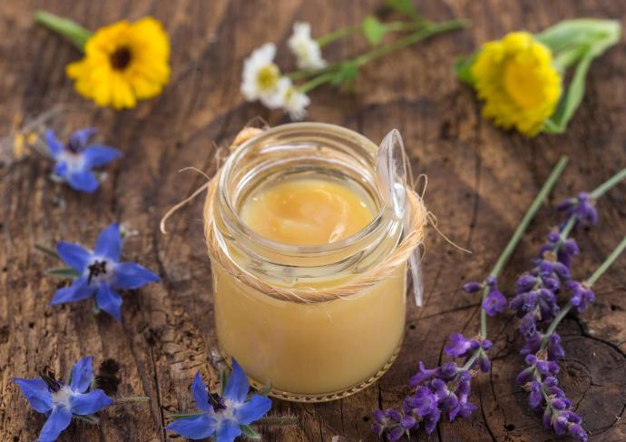 Pot de gelée royale avec cuillère en=n plastique attachée et des fleurs violettes et jaunes autour