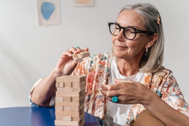 Femme senior lunettes noires qui tient des pièces en bois au-dessus pile de pièces en bois