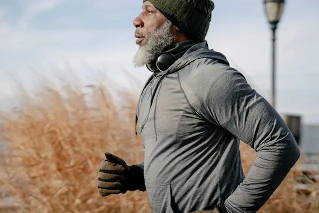 Homme noir senior avec barbe et bonnet et gants de profil qui court