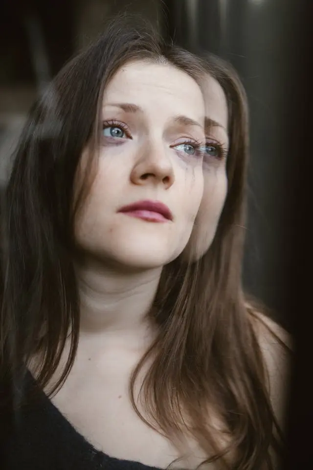 Gros plan visage jeune femme cheveux longs châtains avec mascara qui a coulé qui regarde d'une air triste vers la gauche