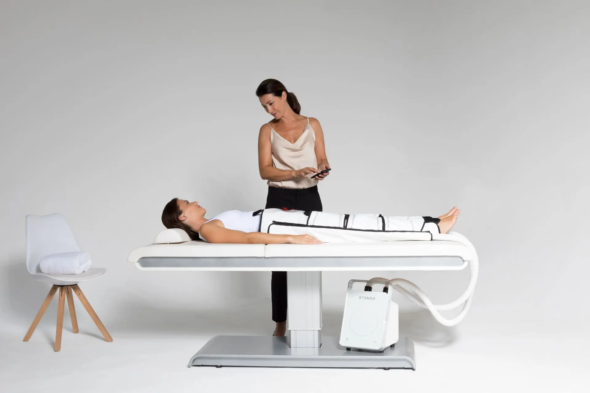 Femme allongée sur table blanche avec machine Strendo® pendant une séance de pulso-thérapie avec femme debout à côté