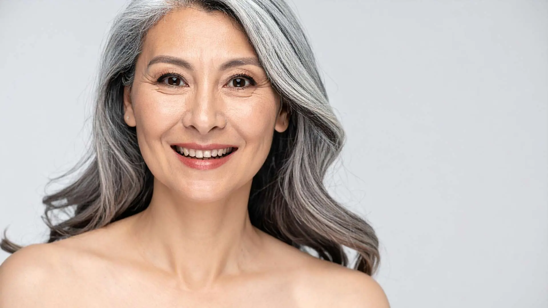 Femme soixantaine aux longs cheveux poivre et sel avec une belle peau qui sourit