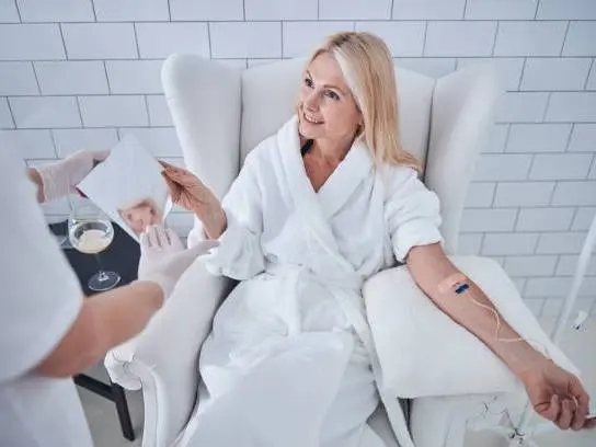 Femme blonde en peignoir blanc souriant pendant une perfusion intraveineuse d'EGCG