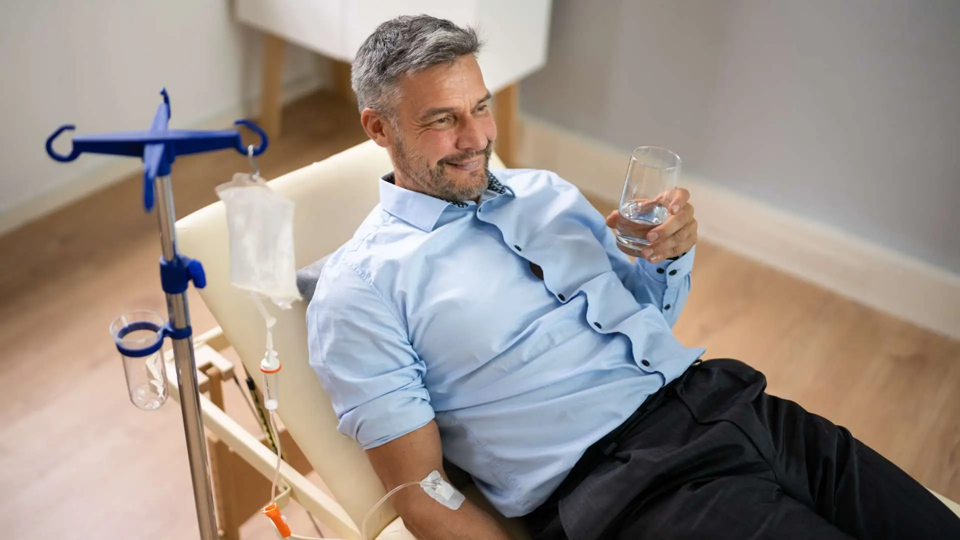 Homme en chemise bleue souriant un verre d'eau à la main pendant une séance de perfusion Intoxication alimentaire