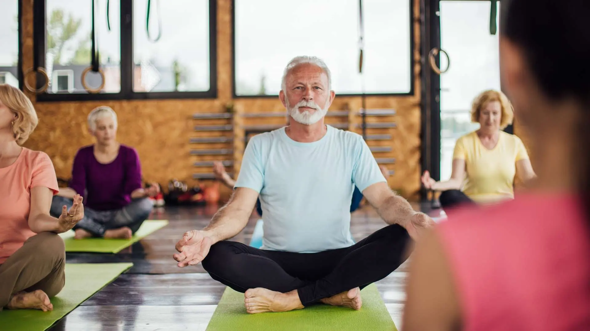 Cours de yoga seniors avec homme barbe et cheveux blancs assis en tailleur au centre