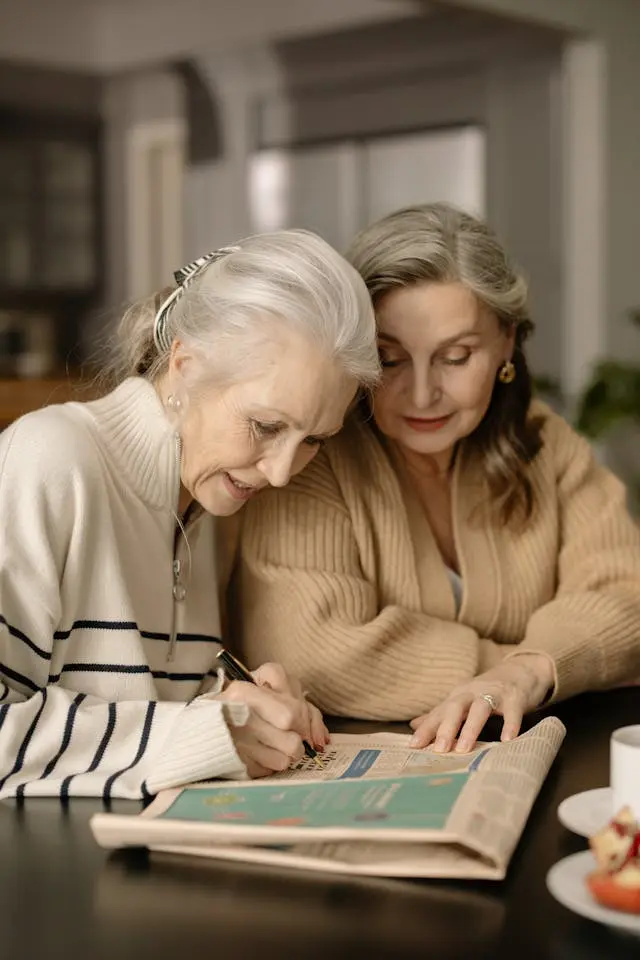 Deux belles femmes seniors assise à une table qui font des mots fléchés sur un journal
