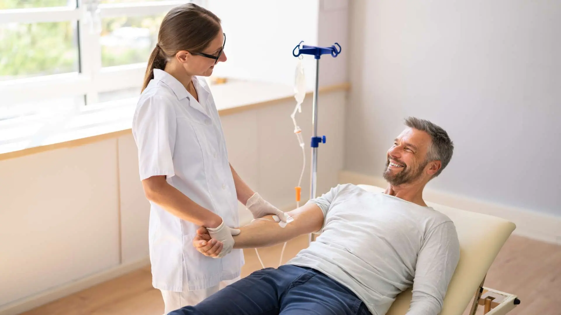 Homme allongé souriant à une femme médecin en blouse blanche pendant séance de thérapie intraveineuse