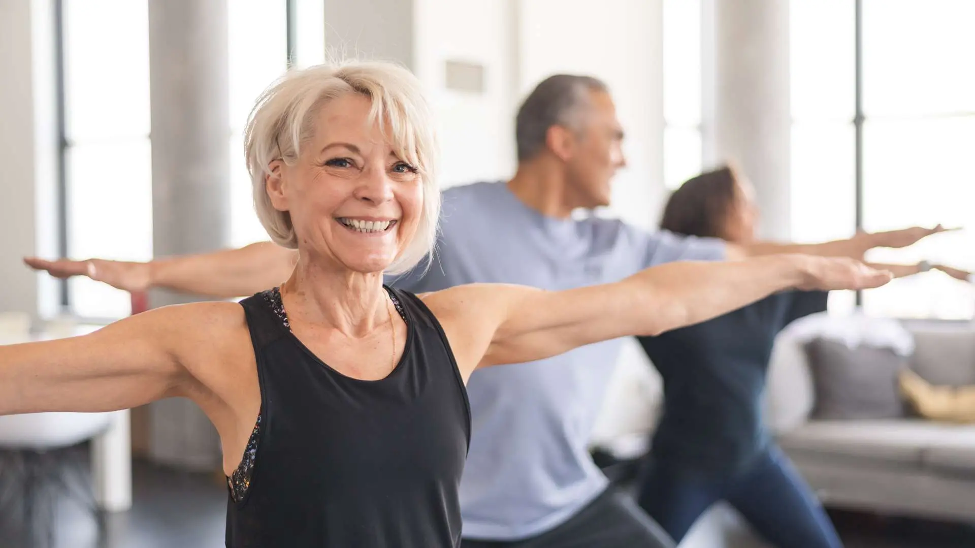 femme senior blonde souriiant pendant cours de Pilates dans une salle avec deux personnes en arrière-plan