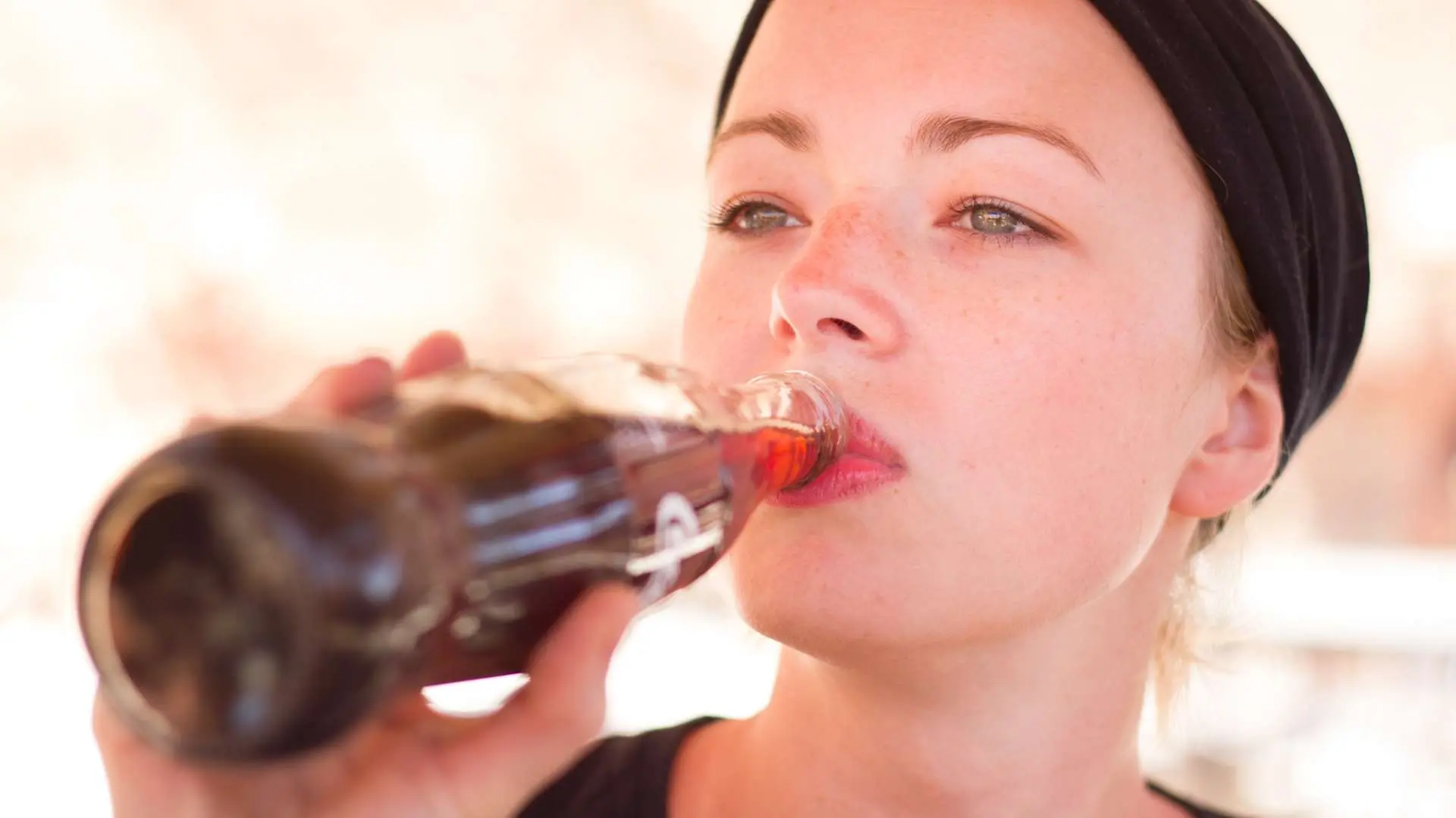 Jeune femme avec un bandeau noir dans les cheveux qui boit  du soda à la bouteille