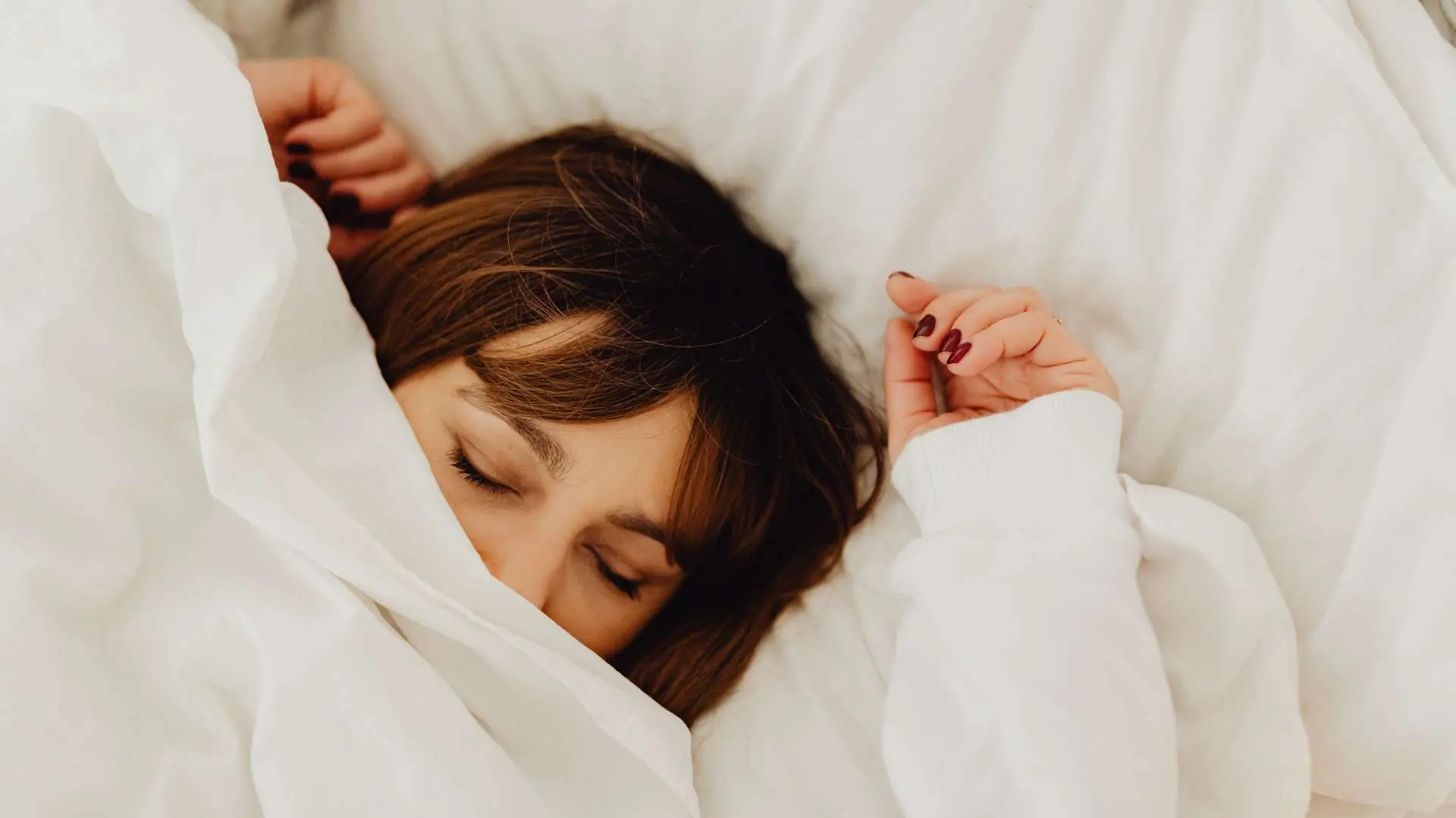 Femme brune qui dort la tête dépassant d'une couette blanche