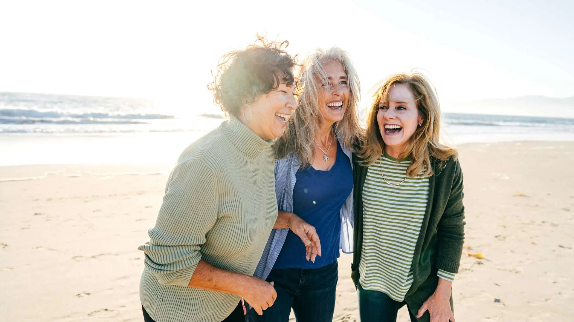 Trois amies qui rient sur la plage avec mer en arrière-plan
